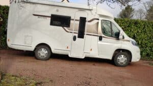 Camping-car blanc stationné devant une haie verte