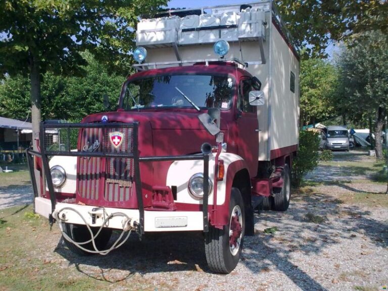 Camion rouge ancien transformé en camping-car, stationné.